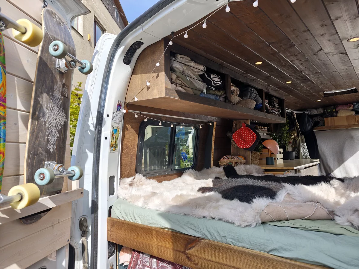 Cosy van interior: wood, sheepskins on the bed, string lights, skateboard on the door